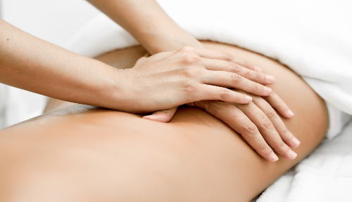 Lower back massage at Cambridge Massage Clinic with lady lying on white comfortable towels.